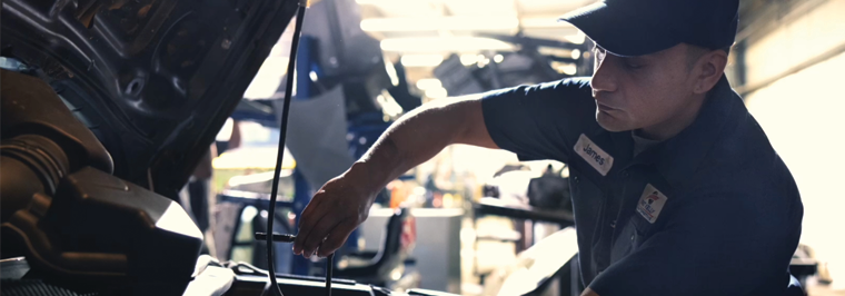 Automotive employee wearing a mechanic uniform working under the hood of a vehicle in auto shop