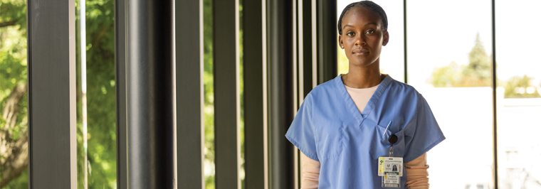 Female healthcare employee wearing blue uniform medical scrubs standing in hallway of clinic